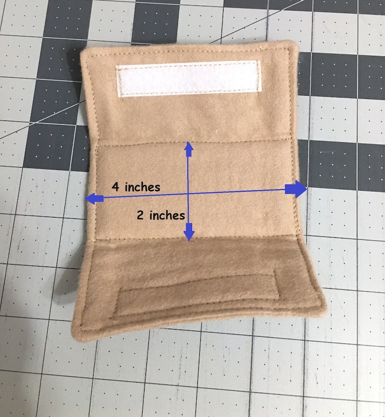 May include: A tan rectangular fabric pouch featuring a white hook-and-loop fastener strip along the top edge. The pouch has a width of 10.16 cm and a height of 5.08 cm, indicated by blue arrows and text labels printed directly on the item.