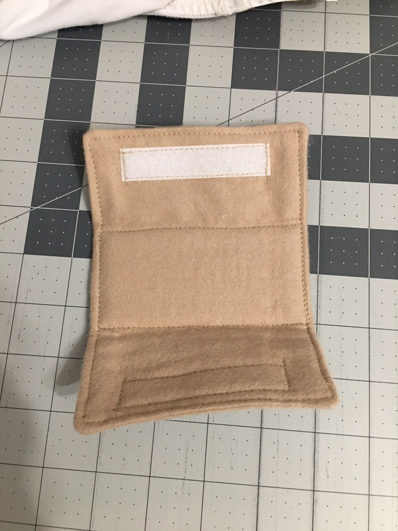 May include: A rectangular tan felt wrap featuring a horizontal white hook-and-loop fastener strip at the top edge and a matching tan hook-and-loop fastener strip positioned along the bottom edge, with visible stitching along all four borders.