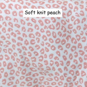 May include: A soft knit fabric featuring a white background with a repeating peach-coloured leopard print pattern. The text Soft knit peach is printed in black on a white rectangular background centred near the top of the image.