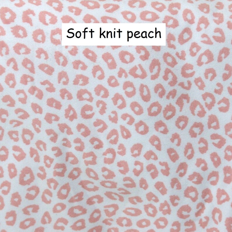 May include: A soft knit fabric featuring a white background with a repeating peach-coloured leopard print pattern. The text Soft knit peach is printed in black on a white rectangular background centred near the top of the image.
