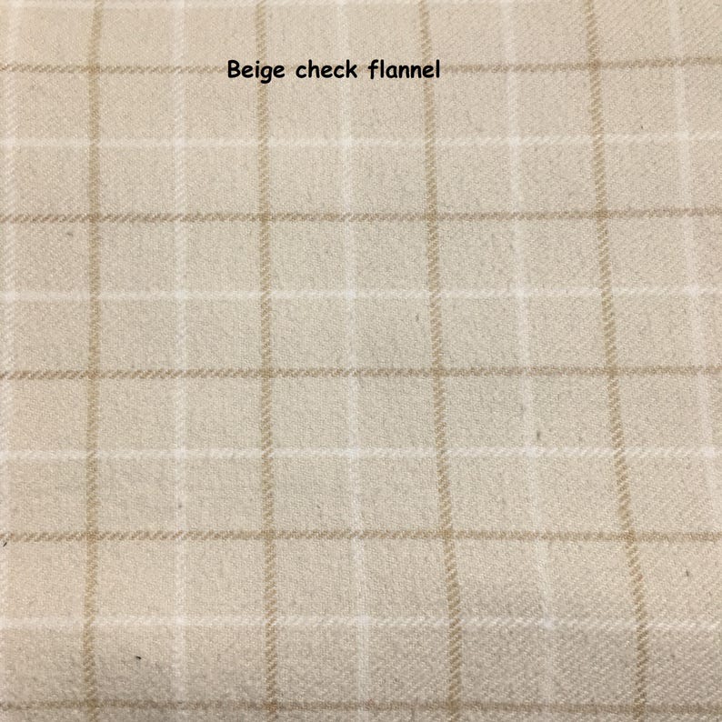 May include: A beige flannel fabric featuring a light brown check pattern. The textile has a soft, brushed texture with a grid design composed of thin, intersecting lines. The text "Beige check flannel" is printed in black at the top centre.