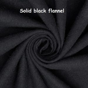 Puede incluir: Primer plano de tela de franela negra lisa. La tela est&aacute; densamente tejida y tiene una superficie suave y ligeramente texturizada. El texto "Solid black flannel" se muestra en letras blancas en la parte superior de la imagen.