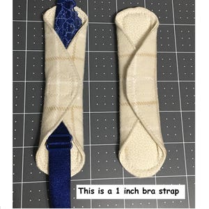 May include: Two beige plaid bra strap covers with a blue strap and lace detail. The text on the image reads: This is a 1 inch bra strap.