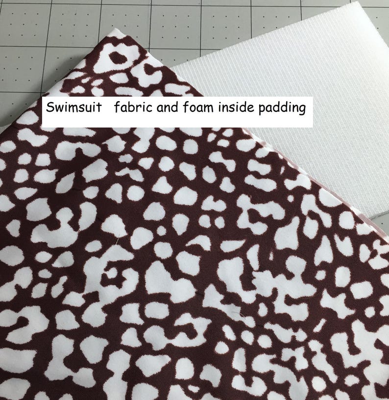 May include: A piece of fabric with a dark brown and white animal print pattern layered over a white foam insert. The text "Swimsuit fabric and foam inside padding" is printed on the fabric surface. The materials are shown in a flat view.