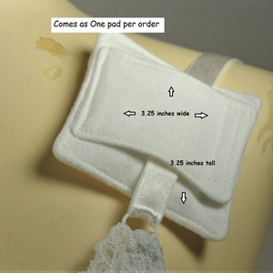 Puede incluir: Una almohadilla rectangular de tela blanca con textura suave, que cuenta con una correa el&aacute;stica blanca unida a la parte inferior. La almohadilla mide 8,26 cm de ancho y 8,26 cm de alto. El texto en la imagen dice: 3.25 inches wide, 3.25 inches tall.