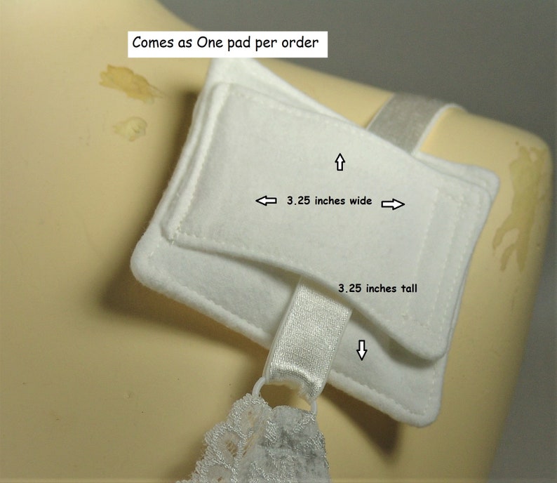 Puede incluir: Una almohadilla rectangular de tela blanca con textura suave, que cuenta con una correa el&aacute;stica blanca unida a la parte inferior. La almohadilla mide 8,26 cm de ancho y 8,26 cm de alto. El texto en la imagen dice: 3.25 inches wide, 3.25 inches tall.
