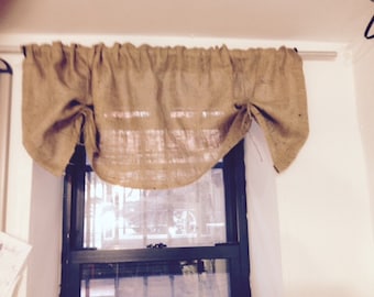 May include: A brown burlap valance hangs on a window rod. The valance is gathered in the center and has a rustic look.