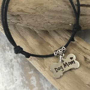 May include: Black cord bracelet with a silver bone charm that says "Dog Mom" with a small heart.