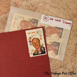 May include: A vintage United States 6&cent; Walt Disney postage stamp featuring a portrait of Walt Disney with cartoon characters. The stamp is affixed to a red textured card. Additional stamps are visible in a clear envelope, with a label reading "10 6&cent; Walt Disney."