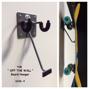 May include: A gray metal skateboard hanger with a black rubber pad on the bottom. The hanger is mounted to a white wall and has a skateboard hanging from it. The text "THE "OFF THE WALL" Board Hanger DKM-4" is printed below the hanger.