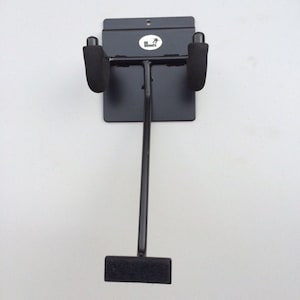 May include: Black metal guitar wall mount with foam padding on the arms. The mount has a black velcro strap at the bottom.