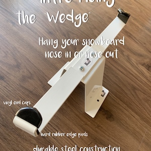 May include: White metal snowboard rack with black rubber end caps and edge pads. The rack is labeled "Introducing the Wedge" and "Hang your snowboard nose in or nose out".
