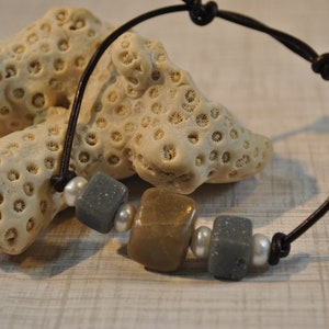Peut inclure: Un bracelet en cuir marron avec des perles carrées grises et brunes et des perles d'espacement blanches.