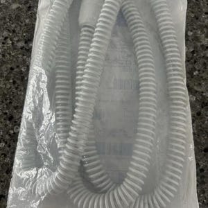 May include: A white, corrugated CPAP tube, coiled within a clear plastic bag. The tube has a ribbed design and is designed for medical use. The bag is sealed and the tube appears new.