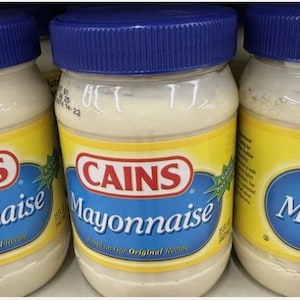 May include: Three jars of CAINS Mayonnaise are displayed. Each jar has a blue lid and a yellow label with the brand name in a red oval and the word "Mayonnaise" in blue. The jars are filled with a creamy white condiment.