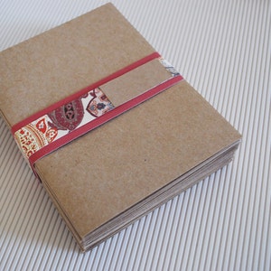 May include: A stack of brown paper envelopes tied together with a red ribbon with a patterned design.