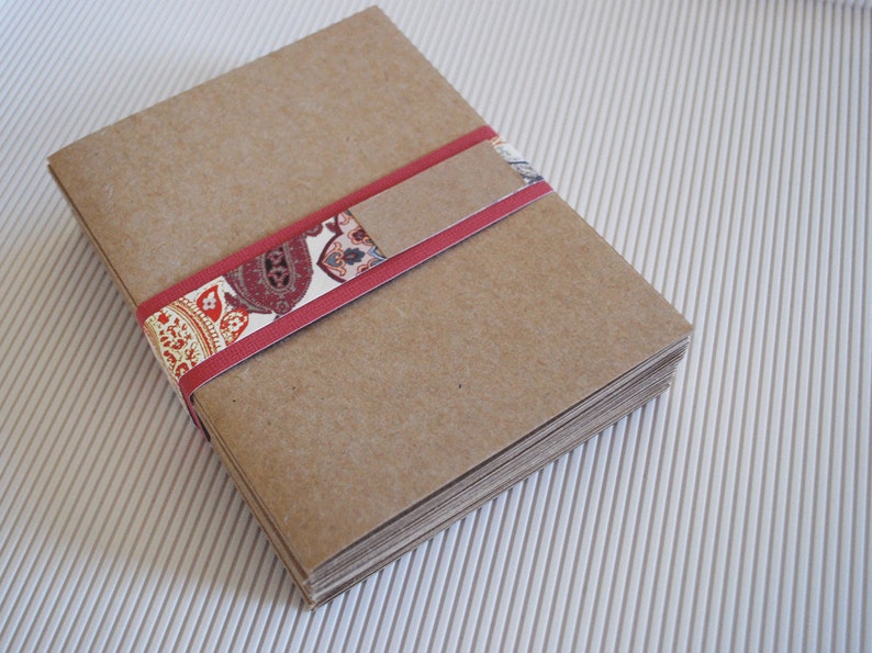 May include: A stack of brown paper envelopes tied together with a red ribbon with a patterned design.