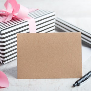 May include: A blank brown card with a black and white striped gift box with a pink ribbon in the background. A black pen is lying on the table.