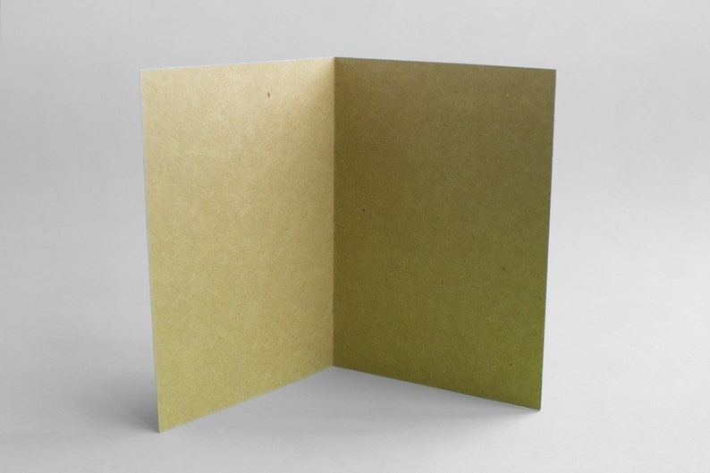 May include: A blank card with a light brown, textured paper surface. The card is folded in half and is open to reveal the inside.