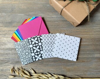 Op de afbeelding: Een set van vier kleine, gepatroneerde enveloppen met zwarte en witte geometrische ontwerpen. De enveloppen zijn gevouwen en gestapeld op een houten oppervlak. De bovenste envelop is roze.
