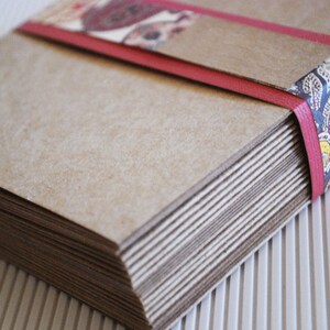 May include: A stack of brown paper cards tied together with a red ribbon and a patterned fabric. The ribbon has a paisley design in blue, white, and yellow.