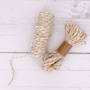 May include: Two spools of twine, one with a brown paper label, both with a white and gold colour scheme.