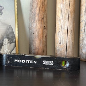 Peut inclure: Un niveau à bulle noir avec les mots "MODITEN SQUIBB" imprimés dessus. Le niveau a une bulle de niveau verte.