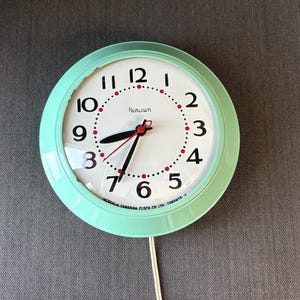 Peut inclure: Une horloge murale ronde vintage avec un cadre vert menthe. Le cadran est blanc avec des chiffres noirs et des accents rouges. Les aiguilles sont noires et rouges. L'horloge indique "Henrun" et "Ingraham Canadian Clock Co. Ltd. Toronto, 12".