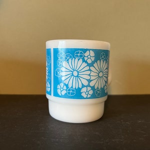 May include: White ceramic mug with a blue and white floral pattern. The flowers are stylized and have a retro look.