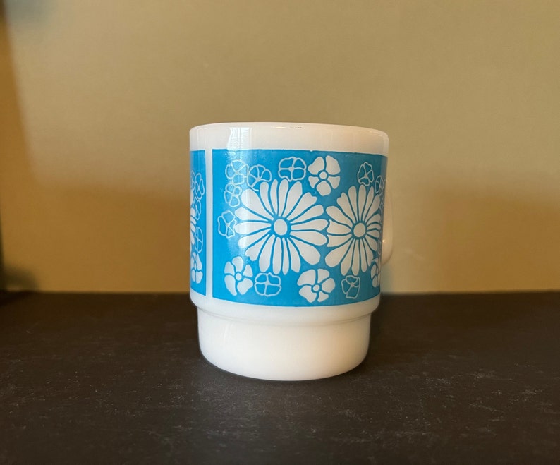 May include: White ceramic mug with a blue and white floral pattern. The flowers are stylized and have a retro look.