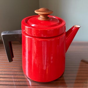 Pu&ograve; includere: Una teiera in smalto rosso vivo con un pomello in legno sul coperchio e un manico nero. La teiera ha un design classico, ideale per preparare il t&egrave;. Il beccuccio &egrave; bordato di bianco.