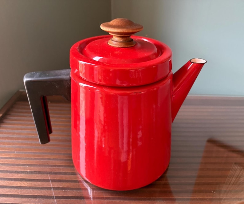 Pu&ograve; includere: Una teiera in smalto rosso vivo con un pomello in legno sul coperchio e un manico nero. La teiera ha un design classico, ideale per preparare il t&egrave;. Il beccuccio &egrave; bordato di bianco.