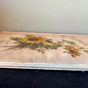 May include: A vintage book with a cream-colored cover featuring a floral illustration of sunflowers and other wildflowers. The title of the book is "Sunflowers" and the text "From the Garden of Hope" is printed on the cover.