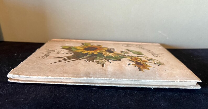 May include: A vintage book with a cream-colored cover featuring a floral illustration of sunflowers and other wildflowers. The title of the book is "Sunflowers" and the text "From the Garden of Hope" is printed on the cover.