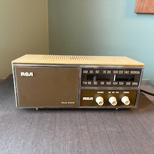 May include: A vintage RCA solid state radio in brown and beige. It has an AM/FM dial, volume, tuning, and AFC knobs. The RCA logo is displayed on the front of the radio.