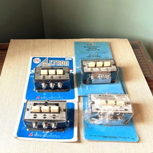 May include: Four vintage video selectors on blue and white packaging. The selectors have silver metal faces with cream-colored buttons and are labeled "Altron" and "Archer". Each unit has multiple input ports.