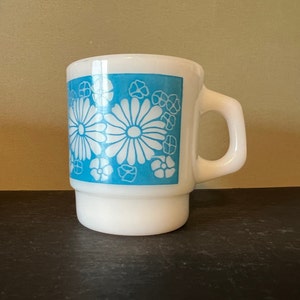May include: White ceramic mug with a blue and white floral design. The mug has a handle and a wide base.