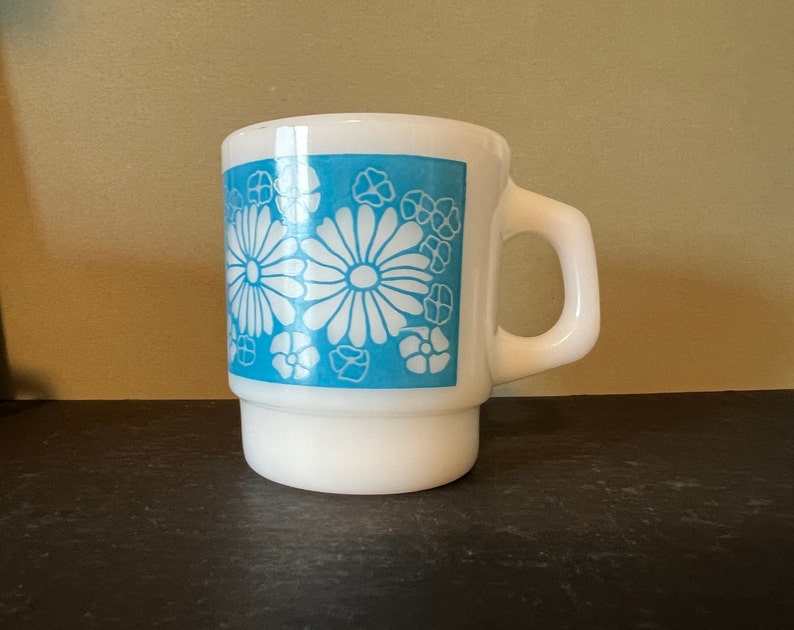 May include: White ceramic mug with a blue and white floral design. The mug has a handle and a wide base.