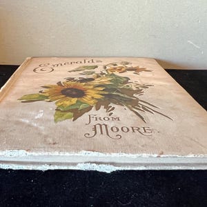 May include: A vintage book with a cream-colored cover featuring a floral illustration of sunflowers and the text "Emeralds From Moore."