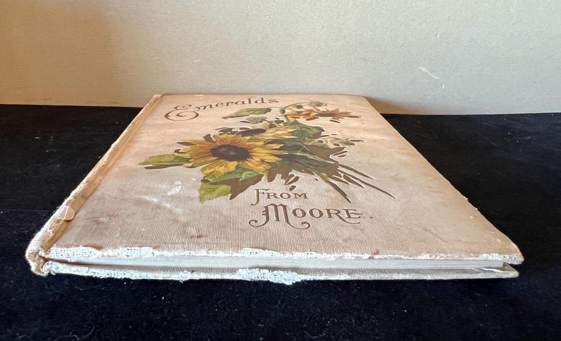 May include: A vintage book with a cream-colored cover featuring a floral illustration of sunflowers and the text "Emeralds From Moore."