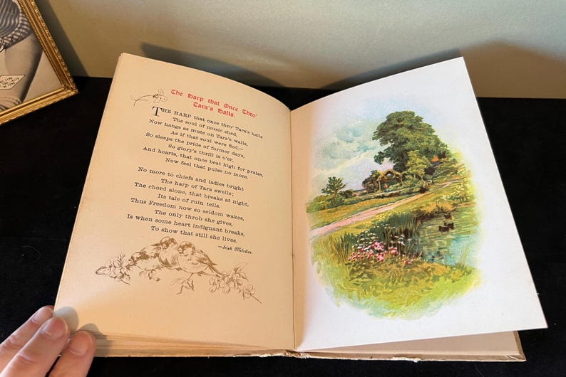 May include: An open book with a poem about a harp and a landscape illustration of a cottage in a green field with a path leading to it. The poem reads "The harp that once through Tara's halls..."