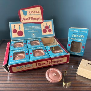 May include: A vintage Revere solid copper utensil hanger display box containing several individual copper circular wall hooks with matching metal hardware, accompanied by a separate blue retail box and a small plain cardboard box.