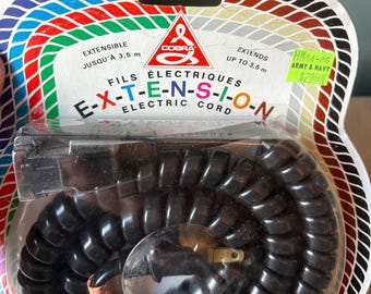 May include: A black coiled telephone extension cord in a clear plastic package. The package has a red, white, and blue striped border. The text on the package reads "COBRA FILS ÉLECTRIQUES E-X-T-E-N-S-I-O-N ELECTRIC CORD EXTENSIBLE JUSQU'À 3.5 m EXTENDS UP TO 3.5 m HW04-86 ARMY & NAVY $299".