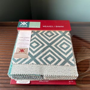 May include: A sample book of upholstery fabric swatches featuring a geometric pattern in shades of blue and white. The book is labelled "Kravet Smart Weaves/Bimini" and "Upholstery #1779".