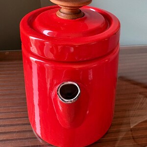 Pu&ograve; includere: Una teiera rosso vivo con un pomello in legno sul coperchio e un beccuccio. La teiera ha una finitura lucida e un design classico. La teiera &egrave; probabilmente in ceramica o smalto.