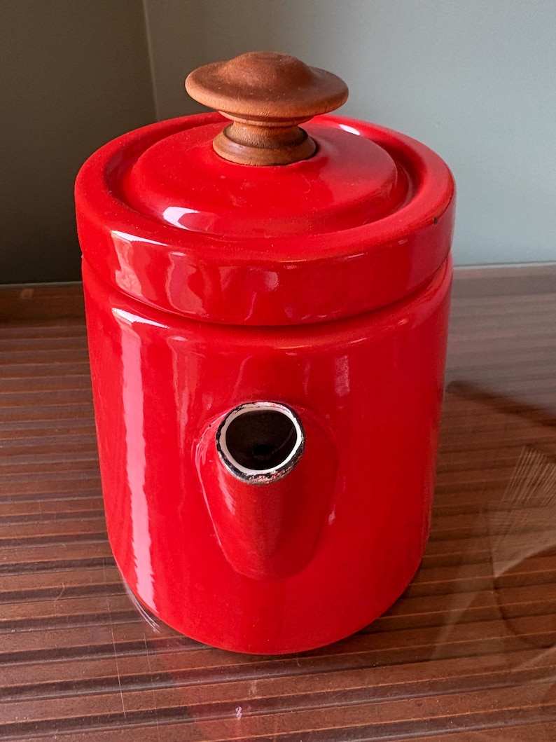 Pu&ograve; includere: Una teiera rosso vivo con un pomello in legno sul coperchio e un beccuccio. La teiera ha una finitura lucida e un design classico. La teiera &egrave; probabilmente in ceramica o smalto.