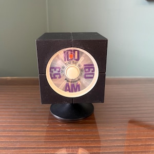 May include: A vintage black Panasonic AM radio with a circular dial. The dial shows radio frequencies from 53 to 160. The radio is cube-shaped and sits on a black base. The word "AM" is at the bottom.