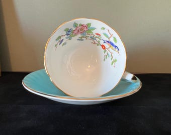 May include: A white teacup and saucer with a blue bird and floral design. The saucer is a light blue color.