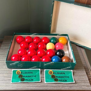 Peut inclure: Un jeu de billes de billard Aramith dans une boîte en carton verte avec le texte Belgian Aramith Balls. Le jeu comprend de nombreuses billes rouges, une verte, une jaune, une rose, une noire, une bleue, une marron et deux autocollants assortis.