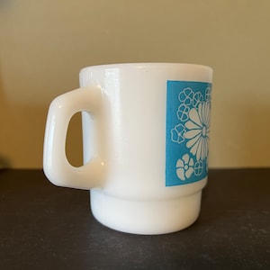 May include: White ceramic mug with a blue floral design. The mug has a handle and a wide base.